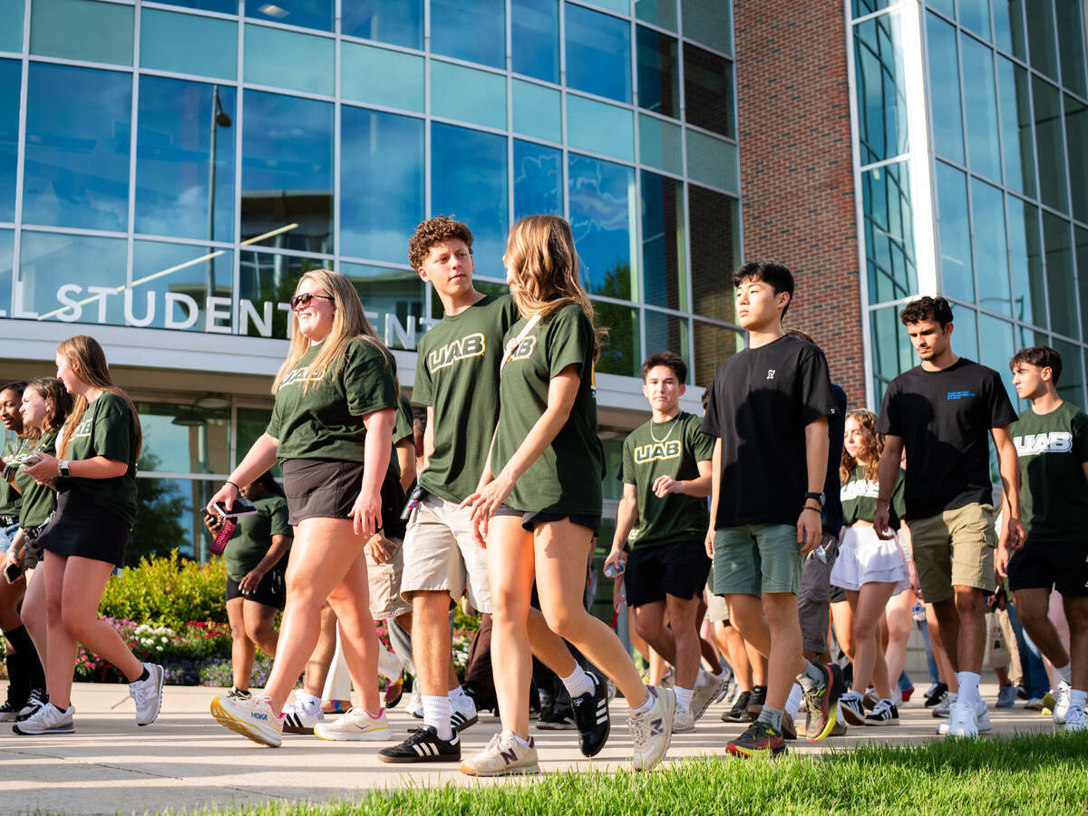 First-Year Convocation, Fall 2025. From side, group of first-year students are walking on sidewalk in front of the Hill Student Center on their way to Bartow Arena