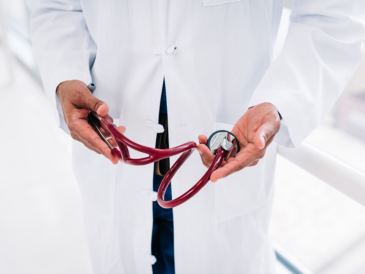 Close-up, the hands of a doctor wearing a white medical coat are holding a red stethoscope.