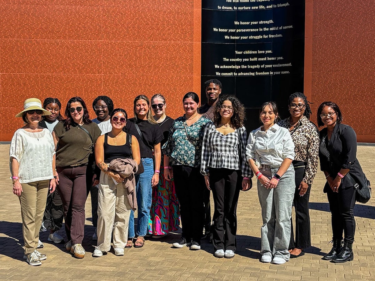 People pose for a photo outdoors on a sunny day in front of a brick wall. 