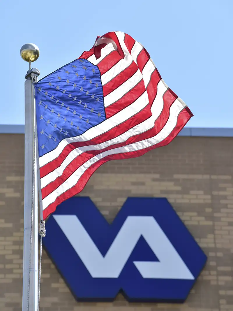 United States flag flying outside VA building with the VA logo in the background