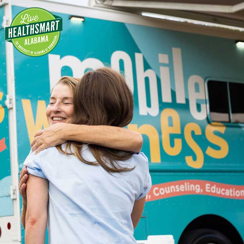 Three female students sitting around a small table with binders and a laptop, in front of a window.