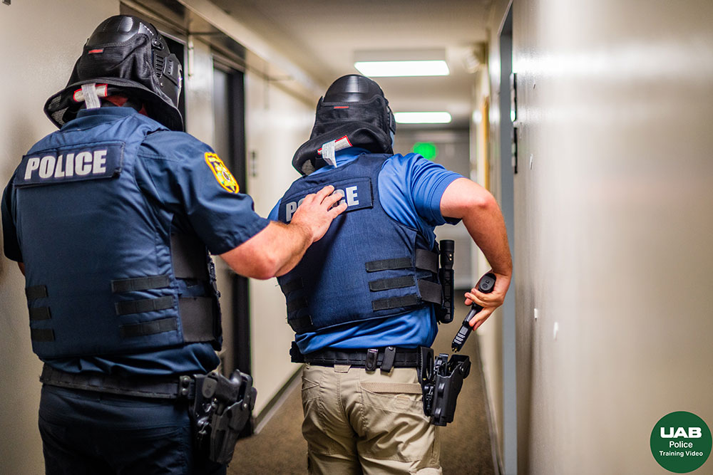 Two police officers wearing bulletproof vests and headgear move down a hallway