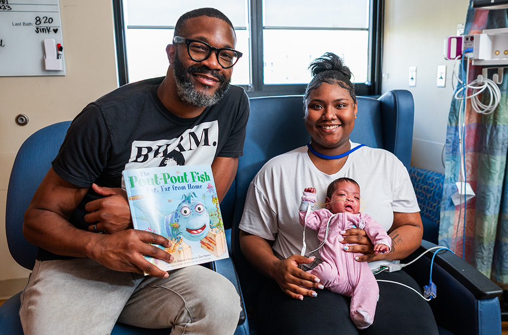 Mayor Randall Woodfin holds a book while sitting next to a mother holding her infant