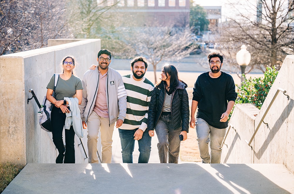 Five students walk abreast up the steps from the Campus Green to the Commons on the Green