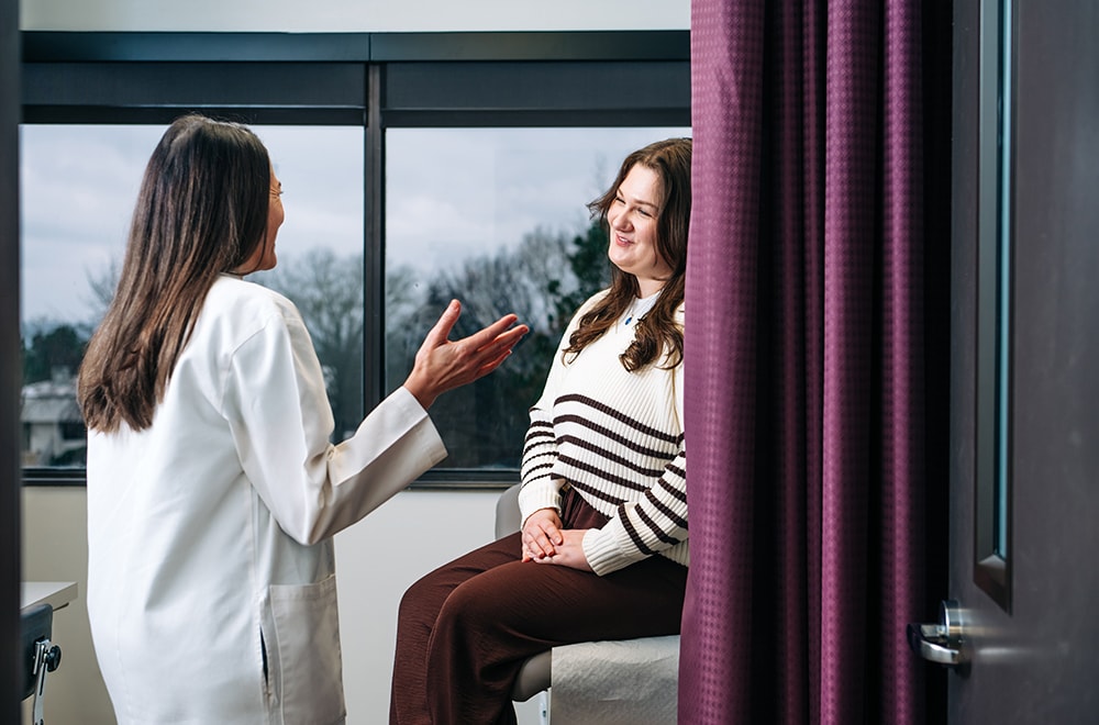A doctor wearing a white coat talks with a smiling patient sitting on an exam table in this posed photo