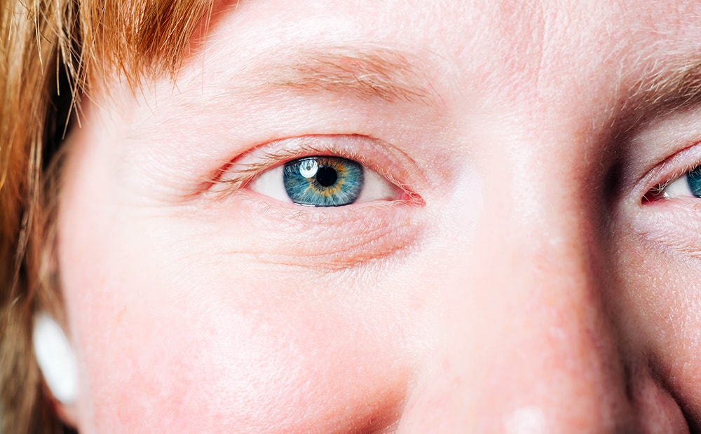 Closeup of an employee's face, focused on her right eye, with a reflection of a light in her iris and red hair visible