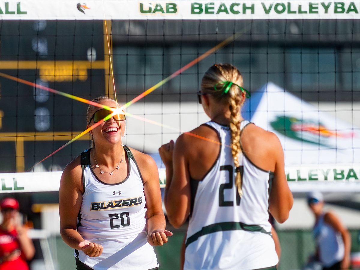 Two UAB Beach Volleyball players celebrate and a ray of light shines off of the player with face to camera