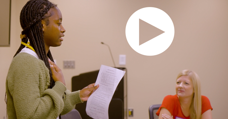 A high school student participating in the Future Public Service Leaders camp reads a report while a faculty member looks on in this still image from a camp video