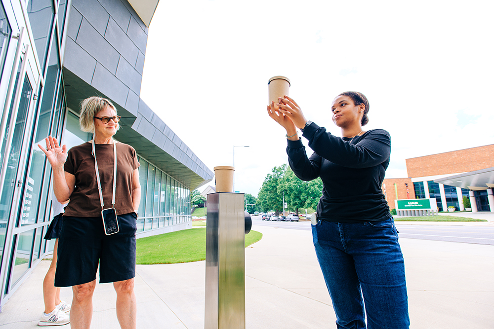 Two participants in the pinhole workshop take selfies with their cameras outside AEIVA with the Alys Stephens Center seen behind them