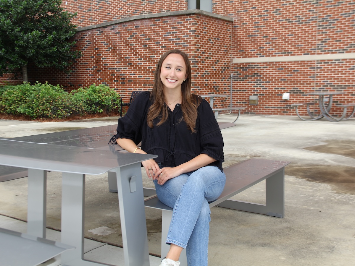 Ellie Prados sitting, legs crossed, at a table outside.