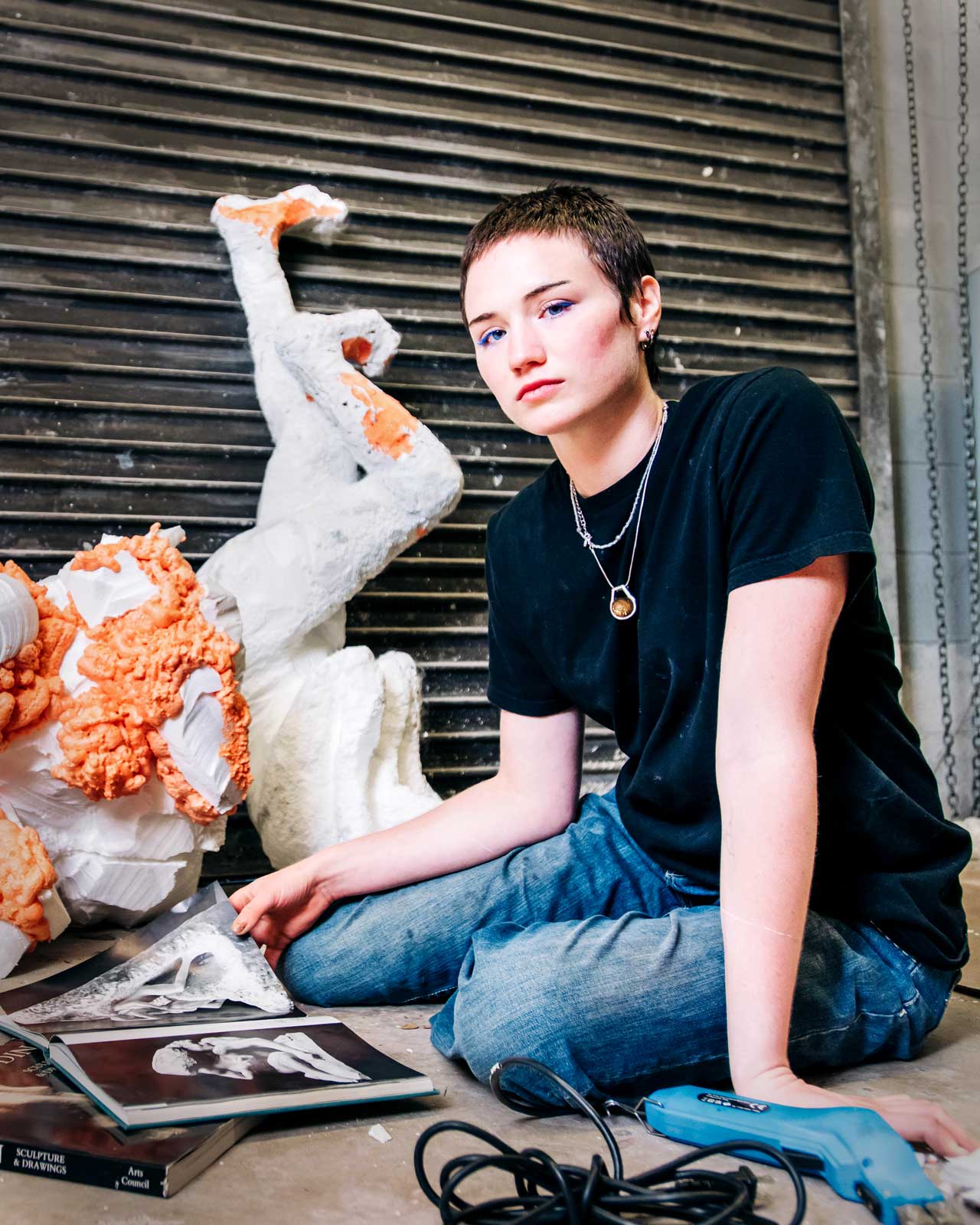 Student sits beside a sculpture while looking through art book.