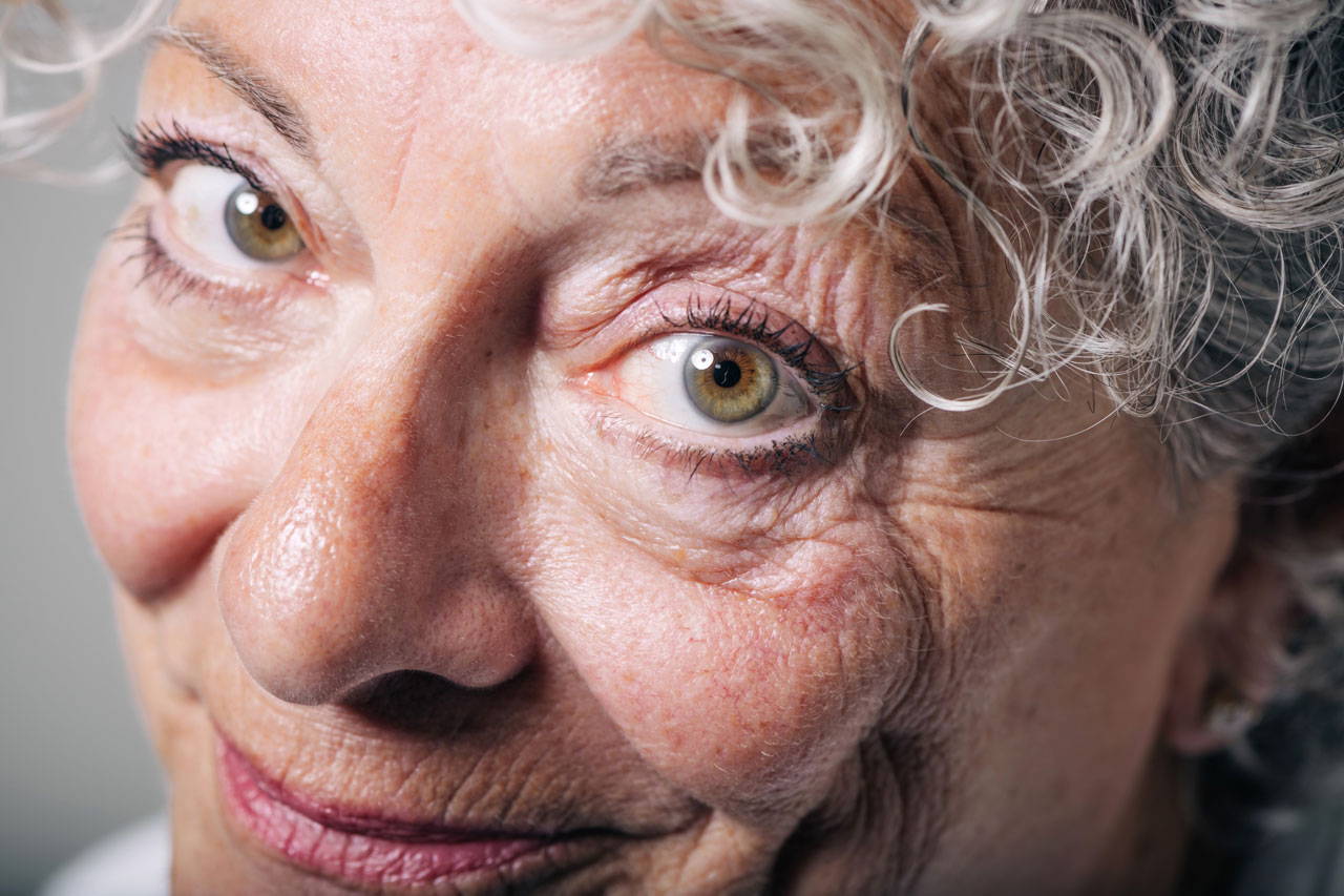 Close-up portrait of an older adult with curly gray hair looking at the camera.